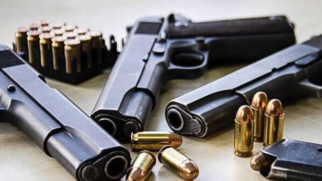 <p>Three pistols laying on table with bullets</p>